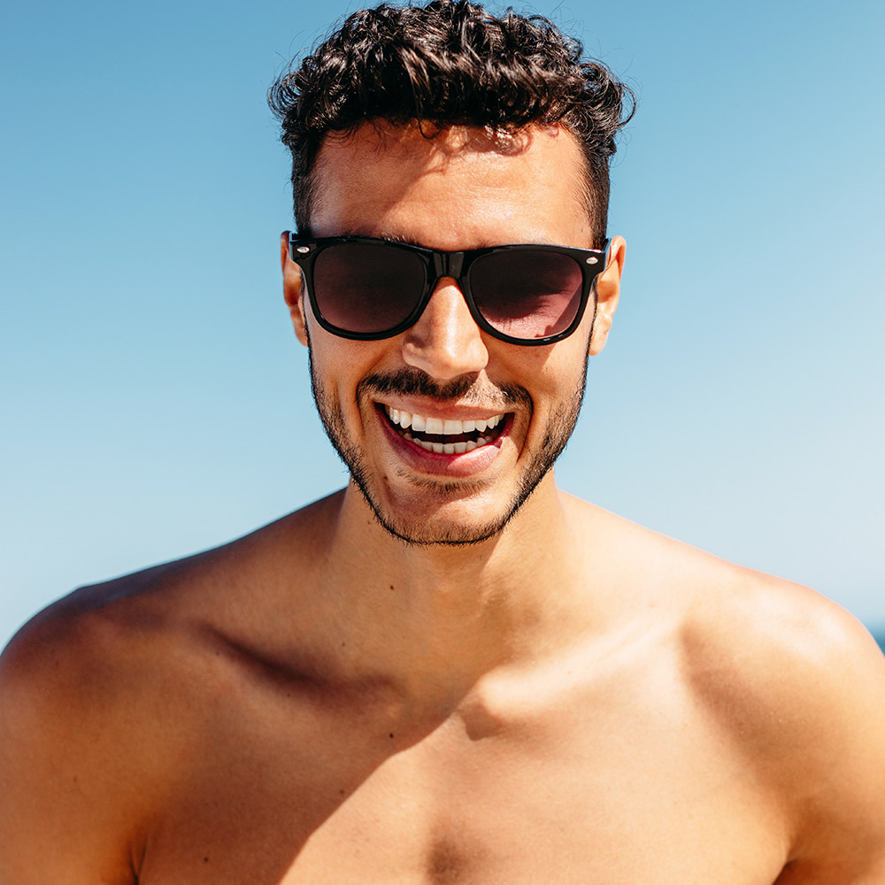 Sunkissed shirtless man in dark sunglasses with open smile
